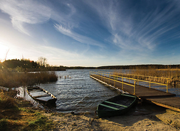 Widok jeziora o poranku – na pierwszym planie dwie łódki przy pomoście i szuwary