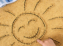 ręka dziecka, które rysuje słońce w piasku na plaży