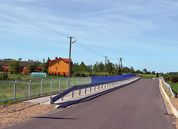 Most z nową nawierzchnią, barierkami i chodnikiem w tle zabudowania gospodarskie