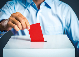 ręka wrzucająca do białego pudła wyborczego czerwoną kartkę