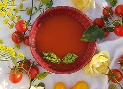 Ujęcie z góry - talerzyk pełen zupy kremowej, obok kwiatki i pomidorki ozdabiające.
