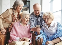 Trzy starsze pani i pan patrzący się w telefon komórkowy