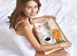 kobieta siedzi na łóżku na kolanach trzyma tacę ze śniadaniem