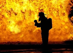 Sylwetka strażaka w stroju ochronnym na tle ogromnego płomienia
