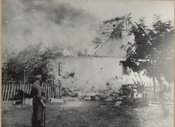 Dwóch żołnierzy z karabinami stojących przed płonącym domem