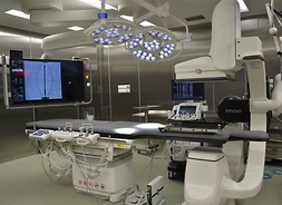 Zdjęcie sali szpitalnej z dużym stołem, ramieniem RTG i wielkim monitorem