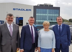 Marszałkowie i dyrektor w eleganckich strojach stoją przed budynkiem fabryki Stadler