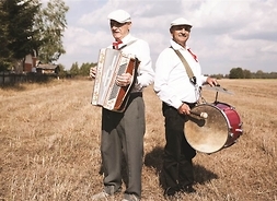 muzycy ze swoimi instrumentami: harmonią i barabanem na tle uprawnych pól