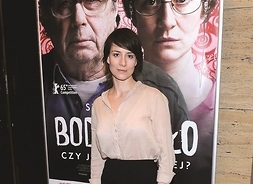 Aktorka przed plakatem zapowiadającym film, z twarzami jej i Janusza Gajosa