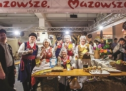 Czworo ludzi w strojach ludowych przed stołem z potrawami regionalnymi i pod szyldem Mazowsze serce Polski