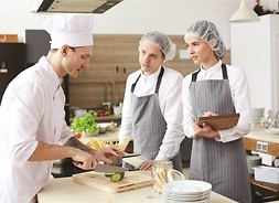 Zdjęcie przedstawia troje kucharzy podczas przygotowywania potraw