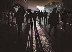 Zdjęcie przedstawia grupę osób idących nocą ulicą