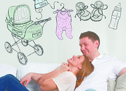 Mężczyzna i kobieta siedzą przytuleni na kanapie, a nad ich głowami umieszczone są rysunki przedmiotów związanych z małym dzieckiem takie jak wózek, butelka z mlekiem, małe buciki