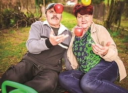 Na zdjęciu mężczyzna z kobietą siedzą na działkowej alejce i podrzucają jabłka
