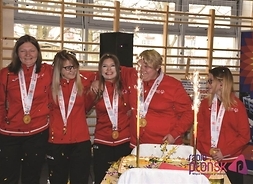 Uśmiechnięte dziewczyny z medalami na szyjach stoją przed tortem