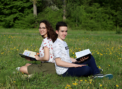 Natalia Matlęga i Karol Kacprzak, stypendyści programu realizowanego przez samorząd Mazowsza, siedzą z książkami w rękach na trawie
