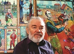 Franciszek Maśluszczak, malarz, rysownik i grafik stoi na tle jednego ze swoich obrazów