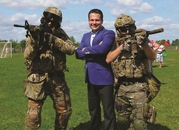 Zdjęcie przedstawia radnego Adama Orlińskiego stojącego pośrodku dwóch żołnierzy