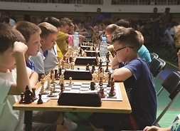 chłopcy grają w szachy, siedzą przy stolikach ustawionych rzędem