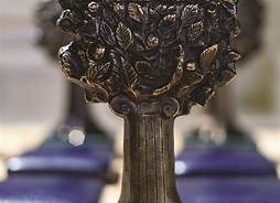 Statuetka przedstawia wykonane z brązu drzewo z pniem w kształcie kolumny w porządku jońskim.