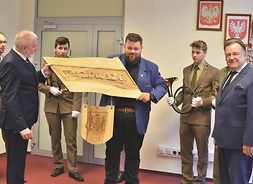 uczniowi szkoły wręczaja marszałkowi własoręcznie wyrzeźbiony logotyp województwa