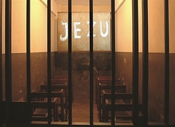 Cela bez okna, krzesła ustawione w rzędach, jedno za drugim, na ściane wyświetlony napis o treści Jezu