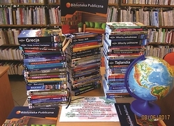 na stole leżą książki ułożone w kolumny, w tle regały z książkami