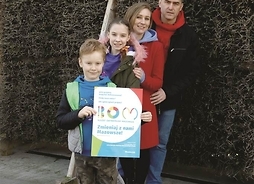 czteroosobowa rodzina pozuje do zdjęcia na tle tężni, w ręku dziecka plakat promujący BOM