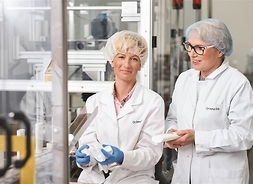 Dwie kobiety w ubraniach ochronnych i czepkach pracują w laboratorium