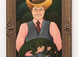 Mężczyzna w kowbojskim kapeluszu, garniturze i krawacie trzyma na rękach małego aligatora