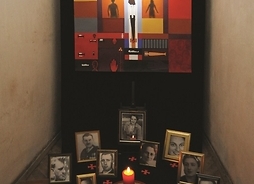 Obraz Chrystusa Ukrzyżowanego na tle wielobrawnych prostokątów. U podnóża obrazu stoją ramki ze zdjęciami pomorodwanych na Pawiaku.