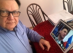 mężczyzna siedzi przy stole, a na nim tablet, na którym prowadzone jest transmisja online