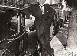Czarno-białe zdjęcie -Tadeusz Sygietyński stoi w pozie zwycięzcy oparty prawą ręką o elegancki samochód.