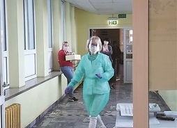 Korytarzem szpitalnym idzie pielęgniarka w fartuchu ochronnym
