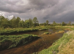 rzeka, a nad nią burzowe chmury, w tle łąki