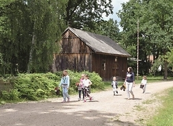 po szutrowej drodze idzie grupa dzieci, w tle drewniana chałupa i drzewa