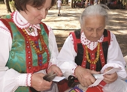 dwie kobiety w strojach ludowych wycinają nożyczkami wycinanki