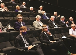 w sali kinowej siedzą ludzie, zachowują dystans społeczny, na twarzach mają przyłbice lub maski