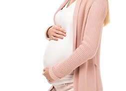 kobieta w zaawansowanej ciąży stoi bokiem obejmuje brzuch, uśmiecha się