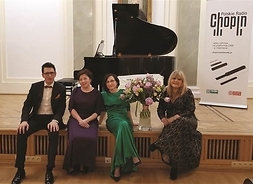 czworo artystów siedzi na scenie w tle fortepian