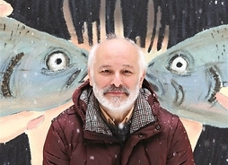 Mężczyzna w zimowej kurtce na tel muralu przedstawiającego dwie ryby stykające się pyszczkami.