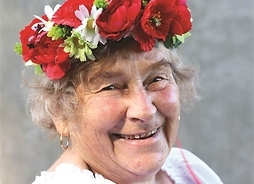 uśmiechnięta seniorka pozuje do zdjęcia, na głowie na wianek z kwiatów