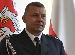 strażak miesiąca pozuje do zdjęcia na tle flag - Polski i samorządu