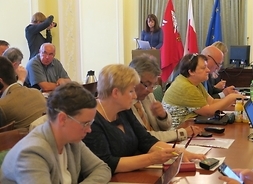 Radni Klubu Platformy Obywatelskiej siedzą przy stole. W tle na mównicy przemawia wicemarszałek Janina Orzełowska