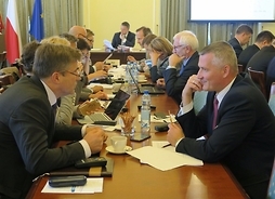 Radni Klubu Platformy Obywatelskiej siedzą przy stole, w tle przy stole prezydialnym przewodniczący sejmiku Ludwik Rakowski