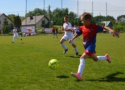 chłopiec w czerwonej koszulce biegnie z piłką w trakcie meczu