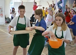 Troje młodych ludzi przyborami kuchennymi na tle pozostałych artystów