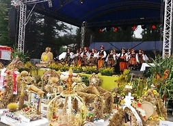 Kilkanaście dużych wieńców ze zbóż i kwiatów przed sceną, na której występuje zespół taneczny