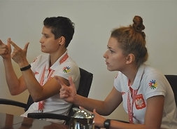 Joanna Kaczmarczyk i Karolina Dampc mówią w języku migowym siedząc przy stole konferencyjnym
