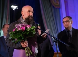 Poeta z kwiatami i statuetką przemawia do mikrofonu